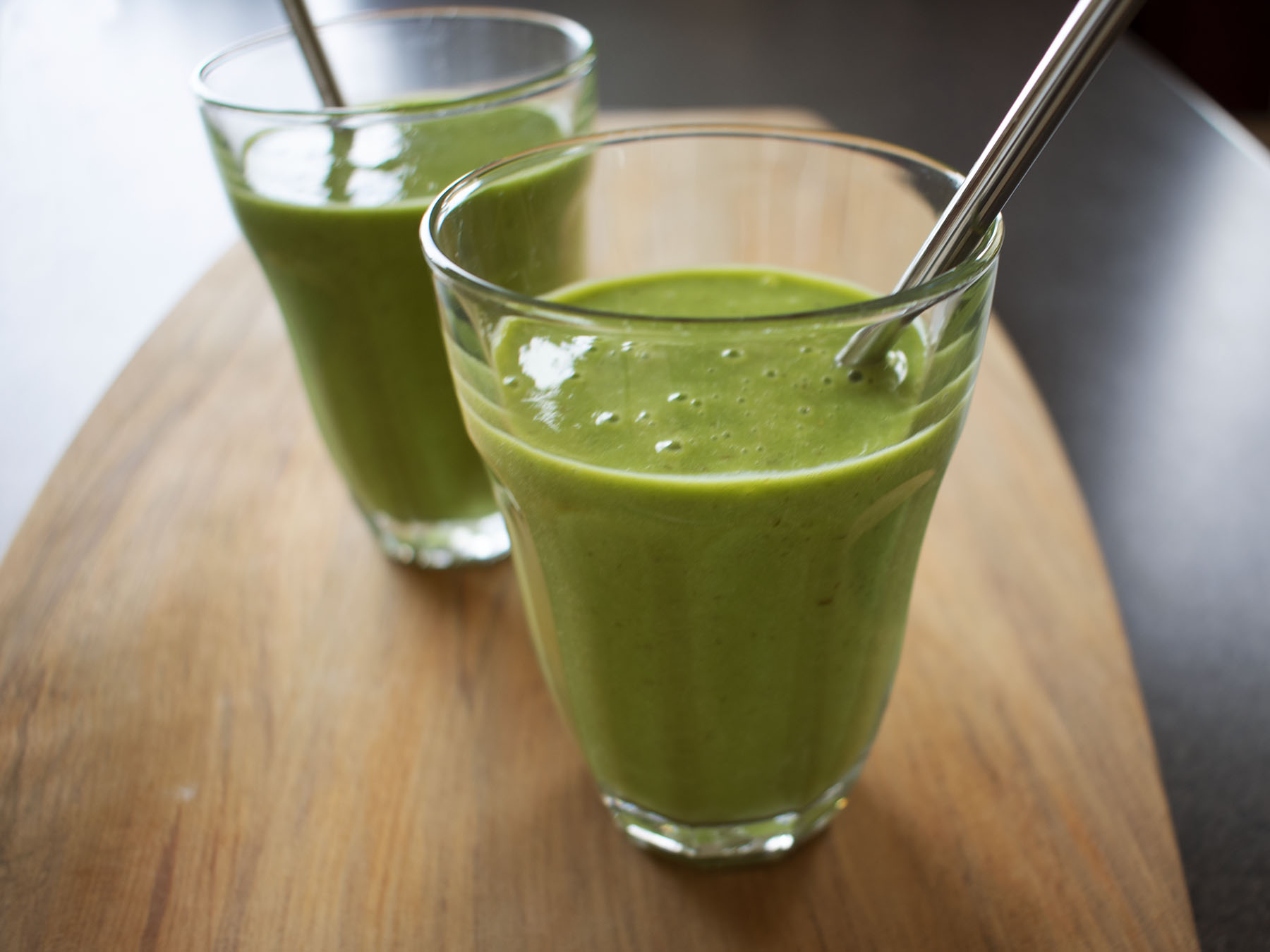 Two small green energy boosting smoothies on wooden board